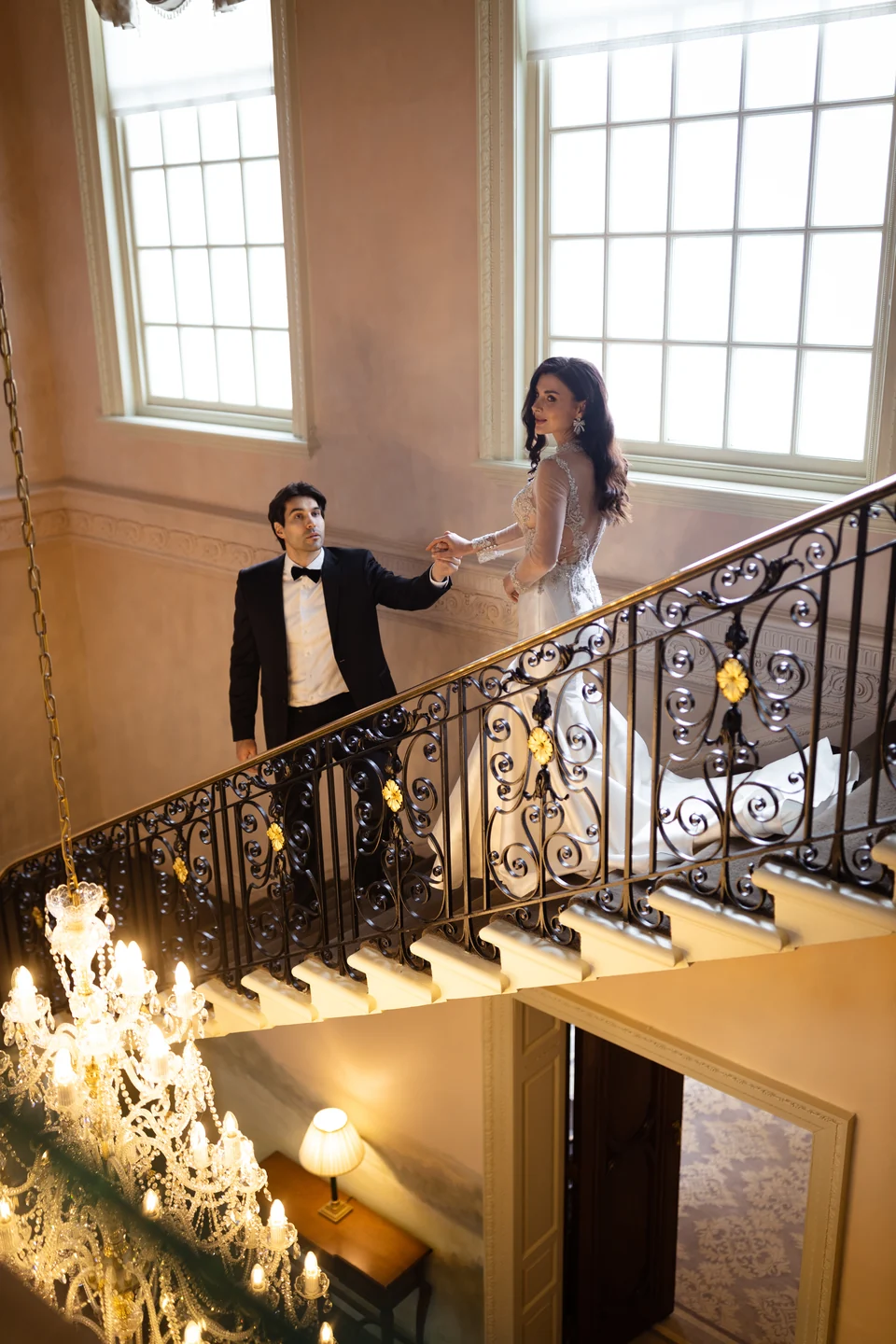 Wedding couple on a sweeping staircase above a chandelier