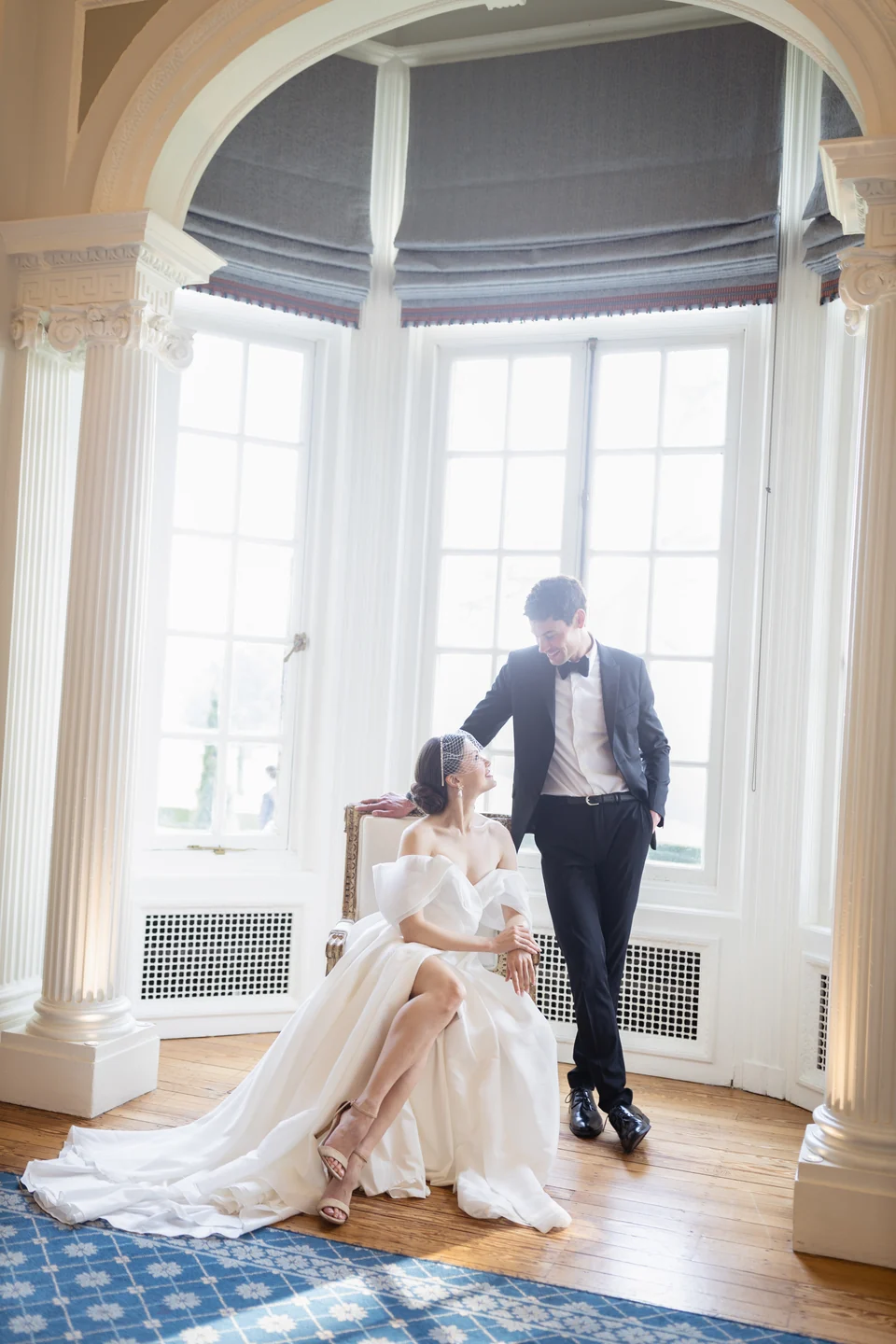 Bride and groom together by a tall bay window