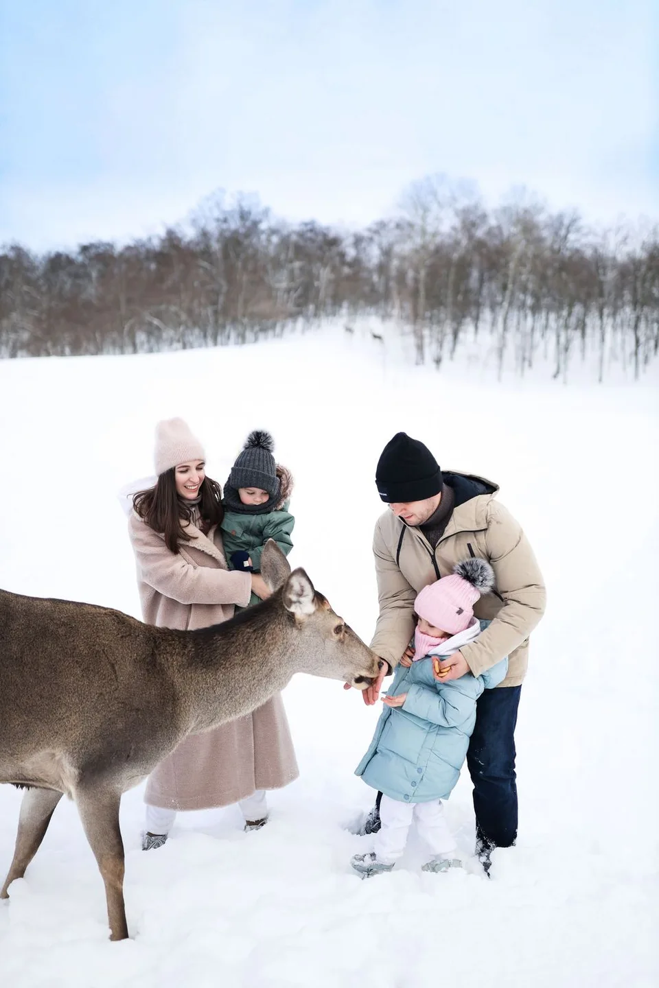 Family feeds wild deer in snowy winter landscape.