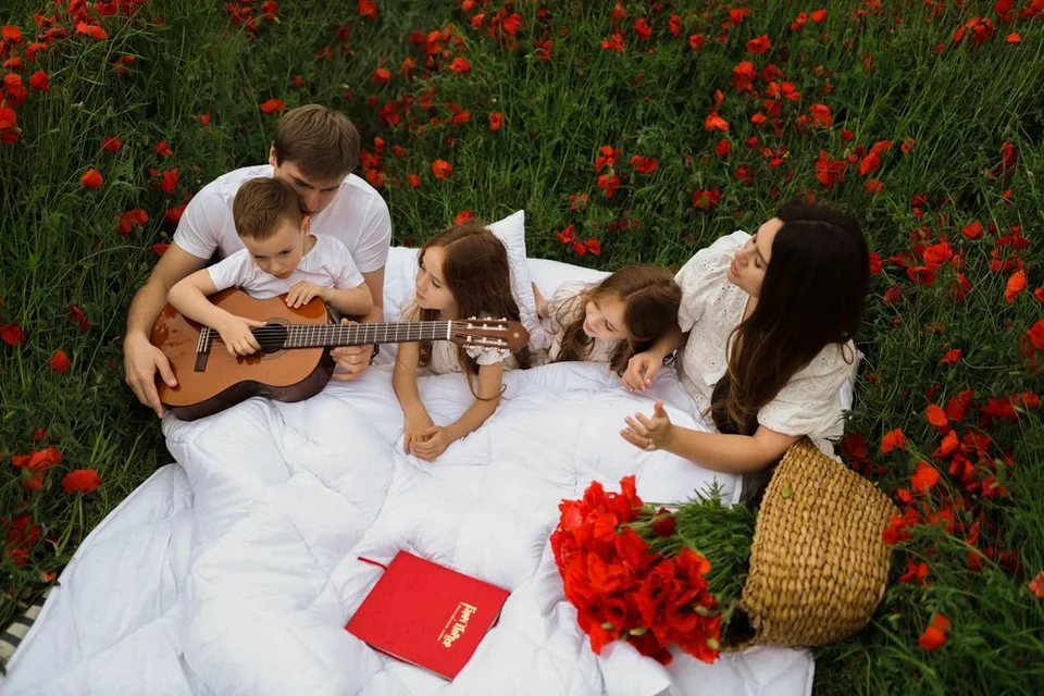 Family having picnic with guitar in red poppy field on white blanket.