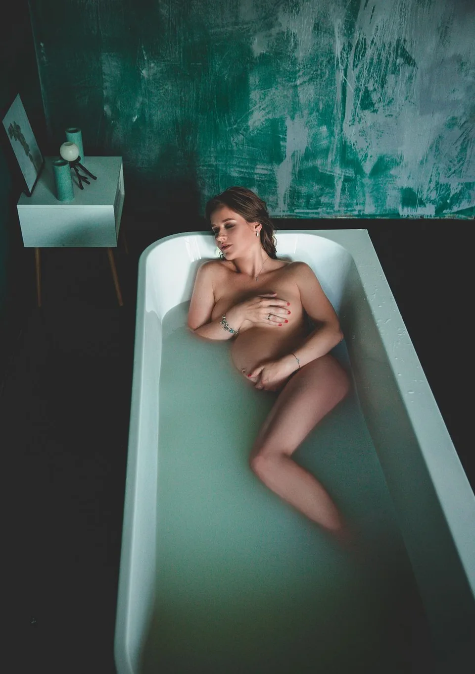Artistic photo of a person reclining in a bathtub against a green textured wall.