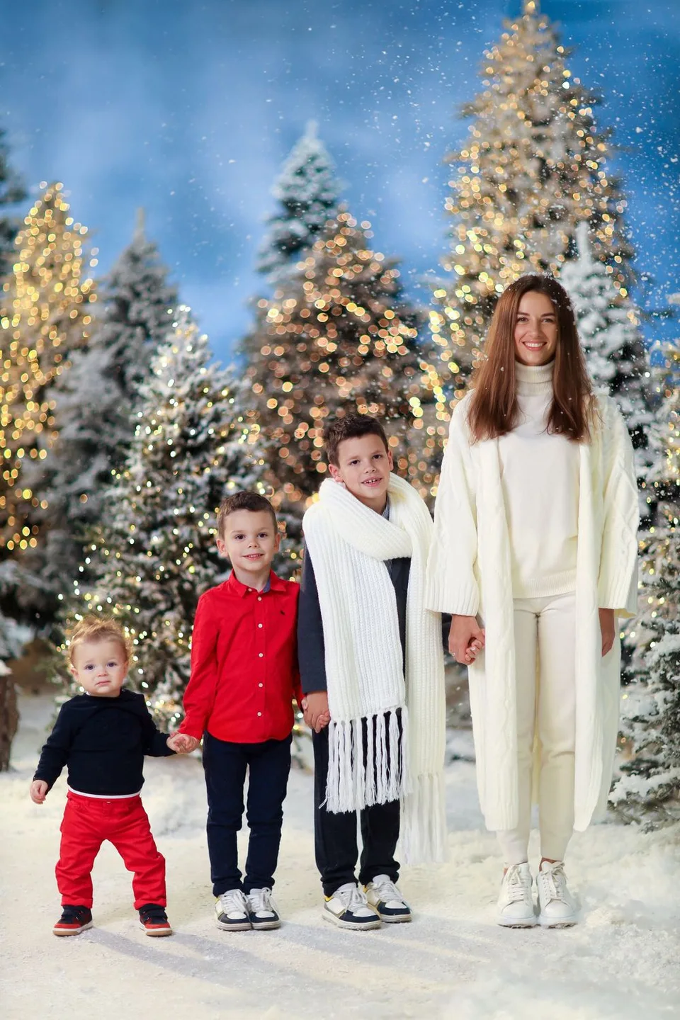 Group in winter outfits standing together against illuminated snowy evergreen trees.