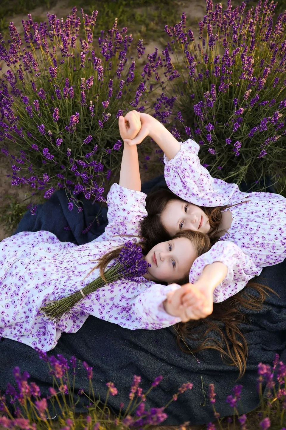 Two people in matching floral dresses lay together peacefully among blooming purple lavender plants.