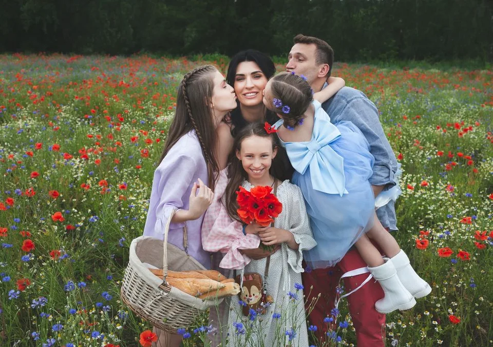 A joyful family moment captured in a wildflower meadow filled with red poppies and blue flowers.