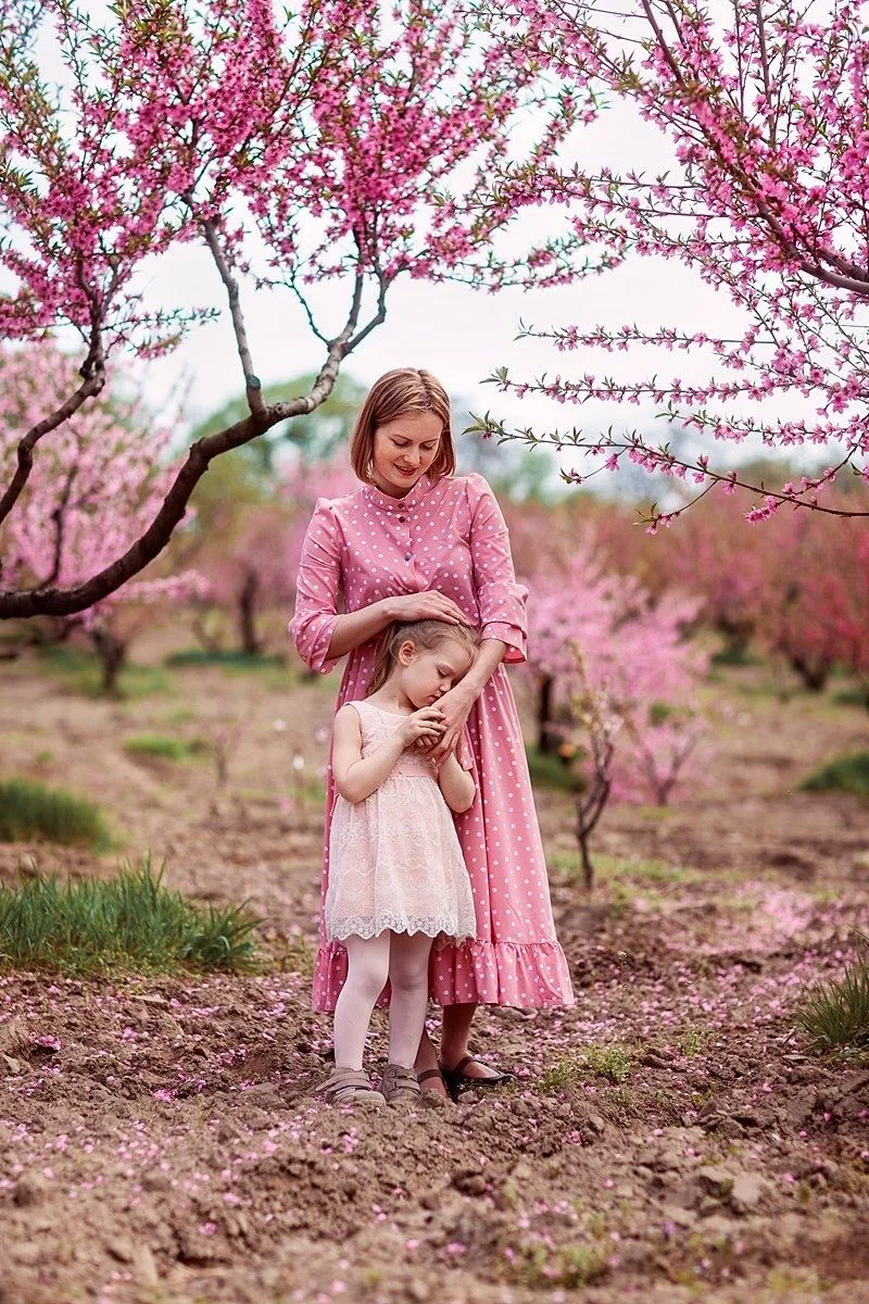 A tender moment under blooming cherry blossom trees with pink spring flowers overhead.
