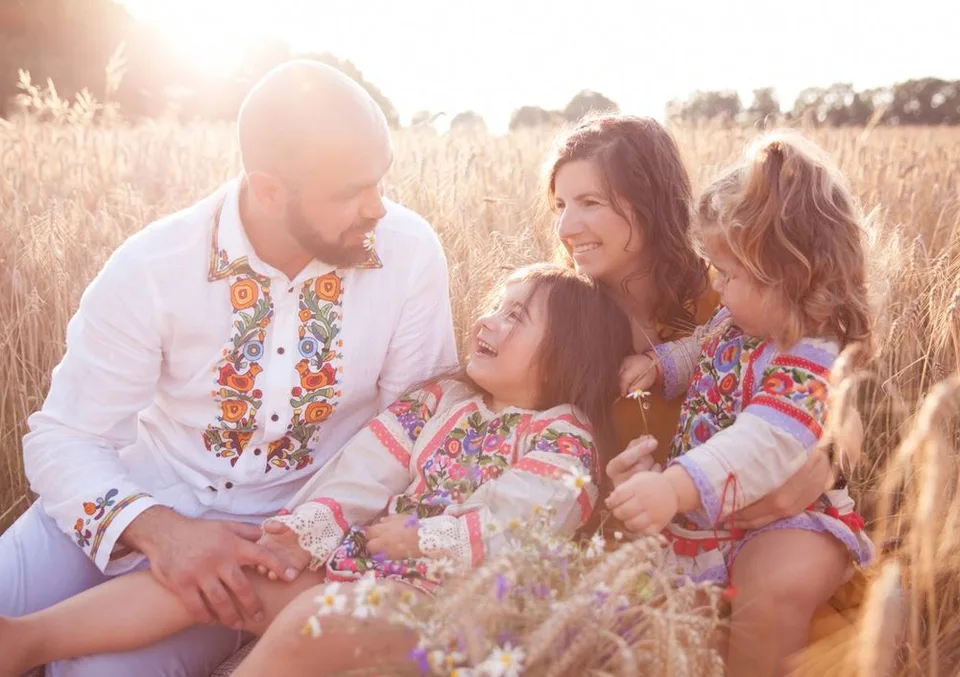 A family wearing traditional embroidered clothing sits together in a golden wheat field at sunset.