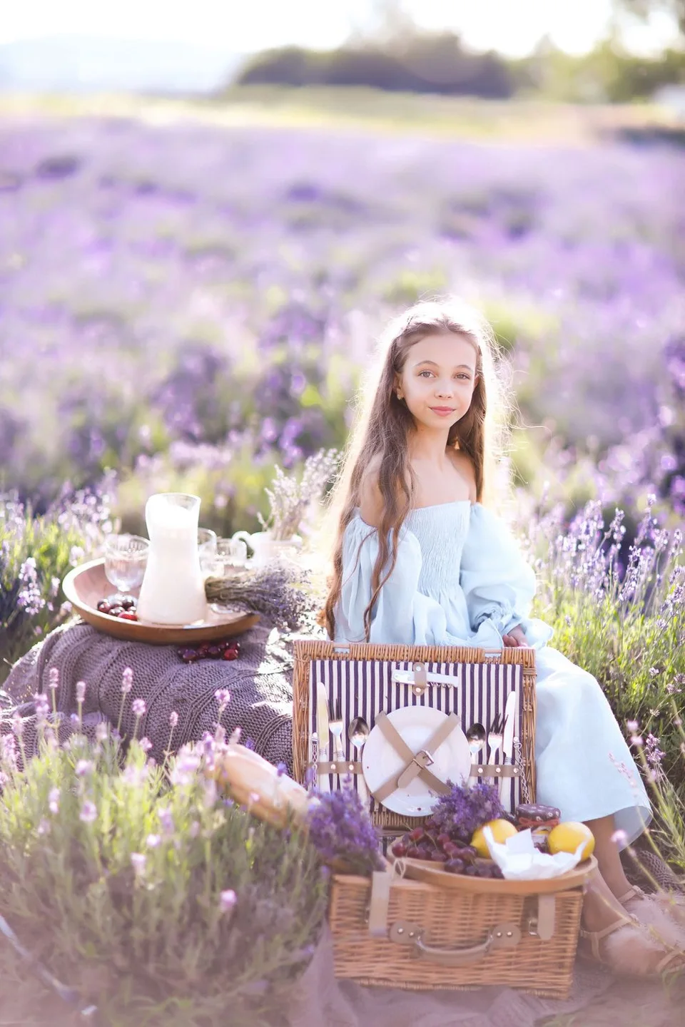 Picnic scene in lavender field with wicker basket and refreshments at sunset.