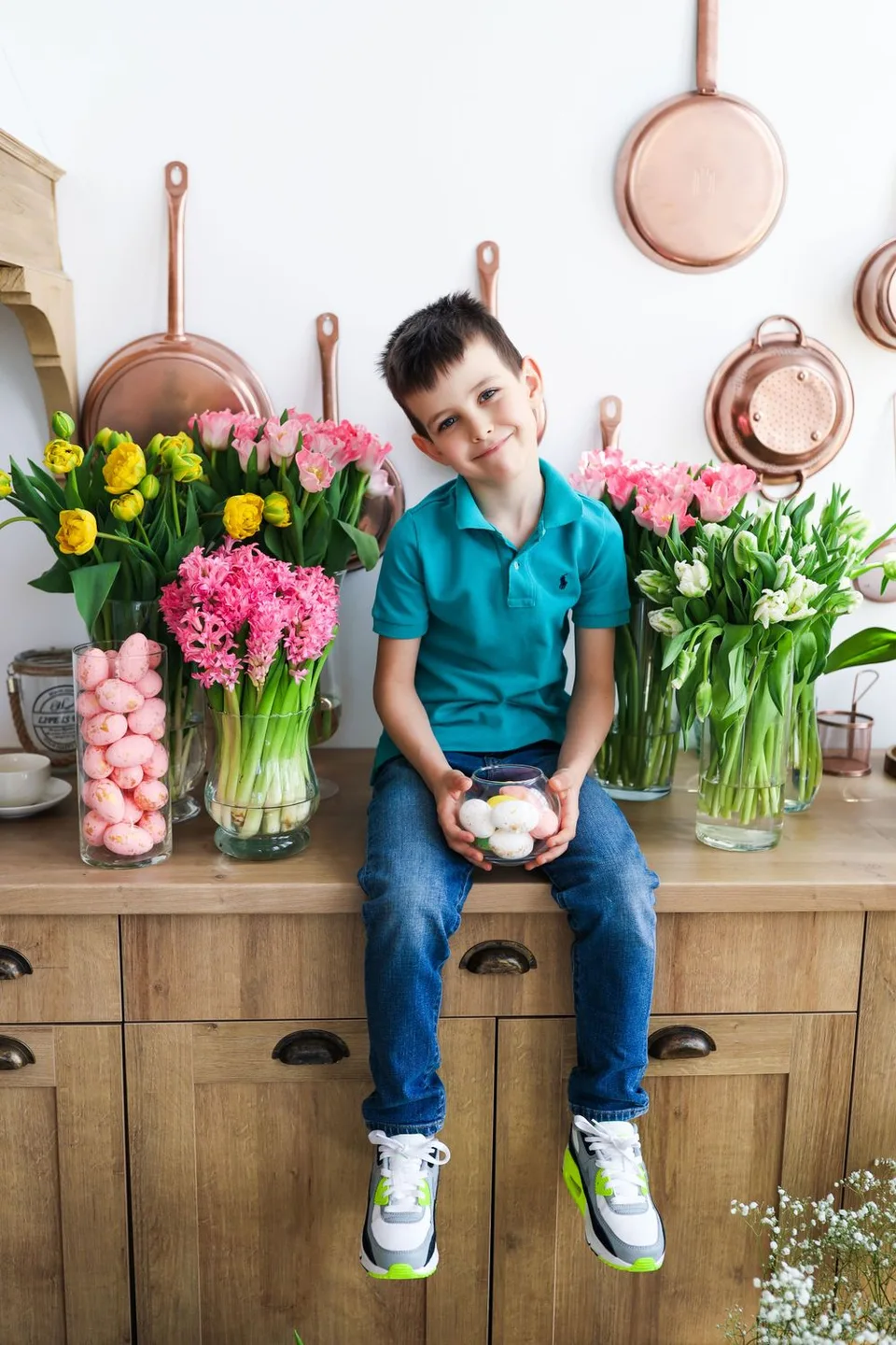 A bright kitchen scene with fresh tulips and copper pans displayed on wooden cabinets.