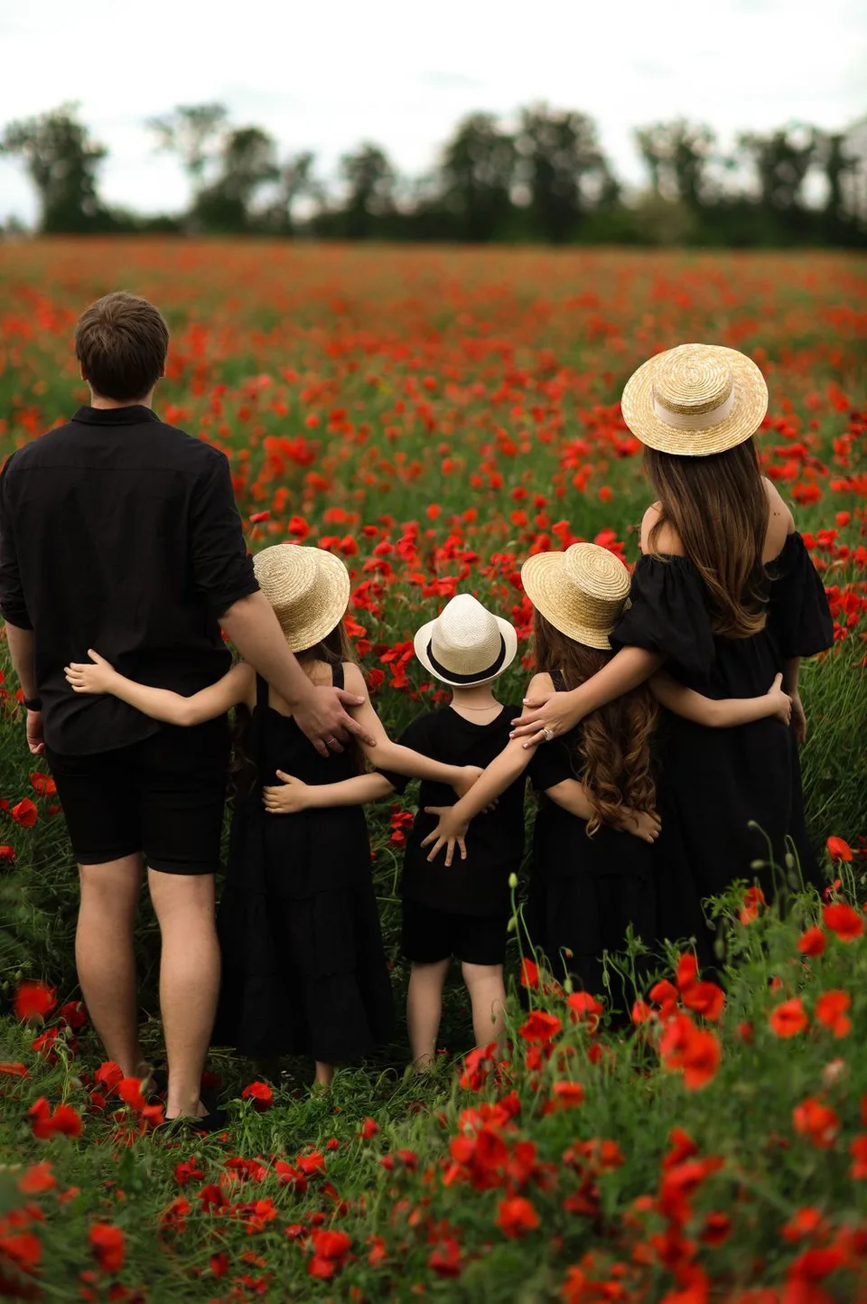 Family in matching black outfits with straw hats standing in red poppy field.