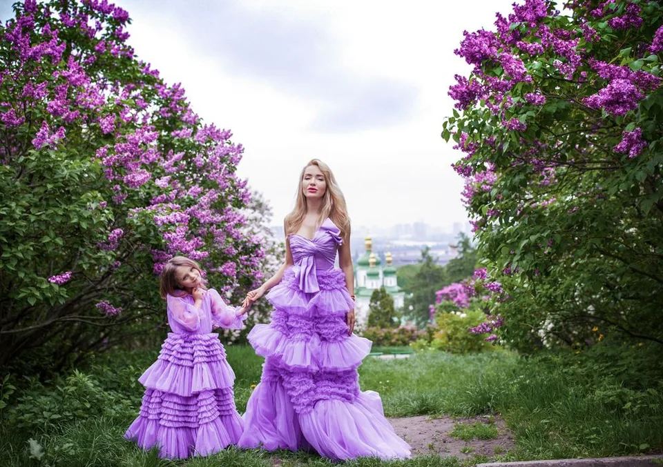 A magical garden scene with two people wearing matching purple tiered dresses among flowering trees.
