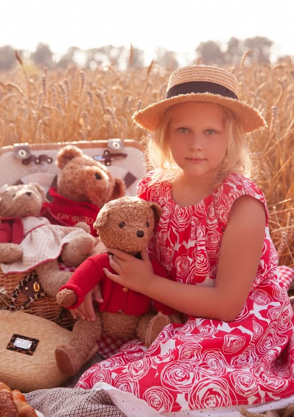 A picturesque picnic scene with teddy bears and red dress in a golden wheat field.