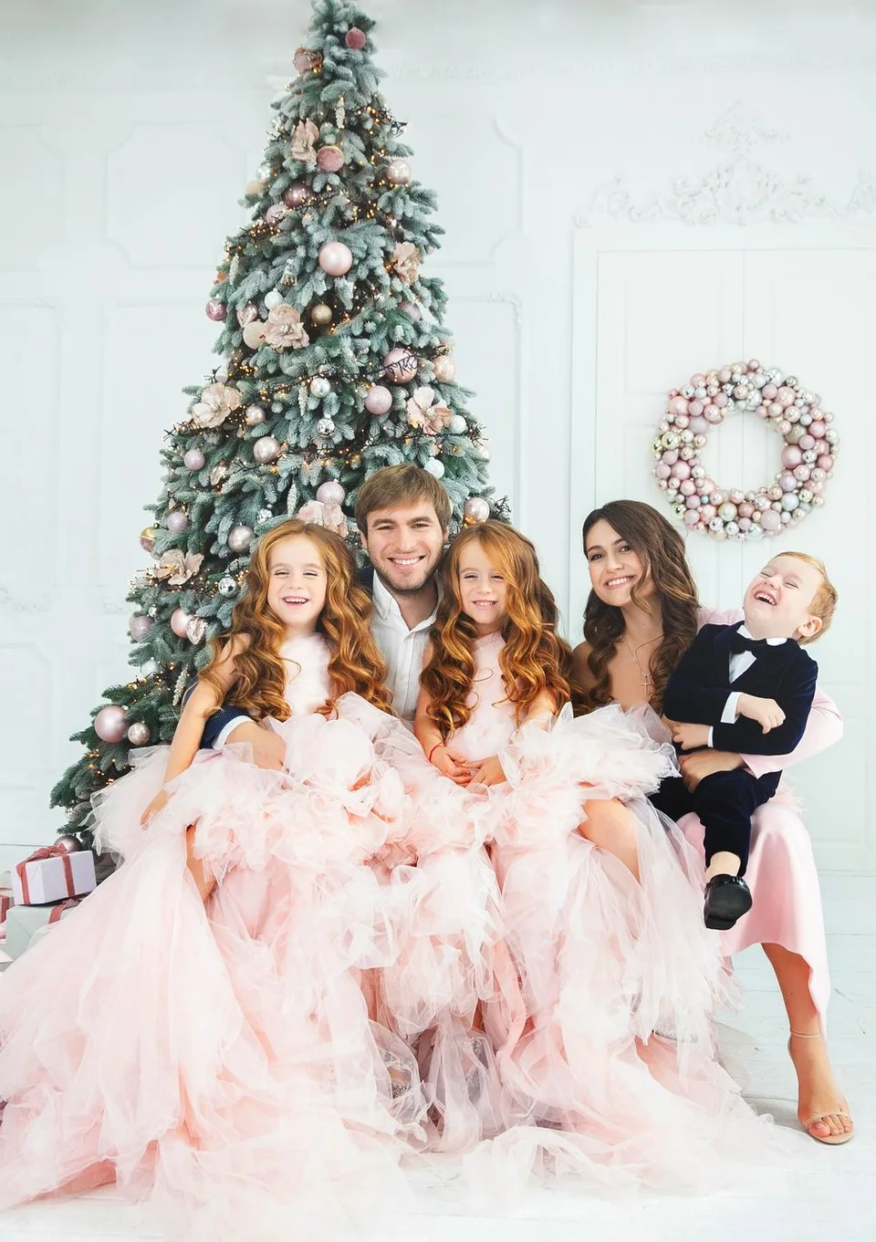 Elegant holiday portrait in front of a decorated Christmas tree with pink tulle dresses.