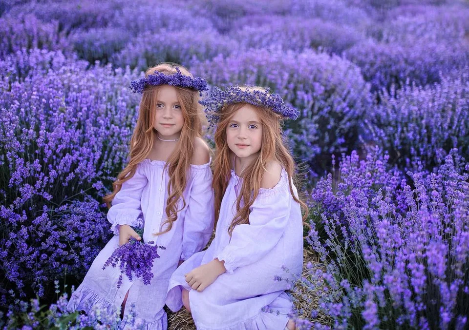 Two children wearing purple dresses and floral crowns pose in a lavender field.