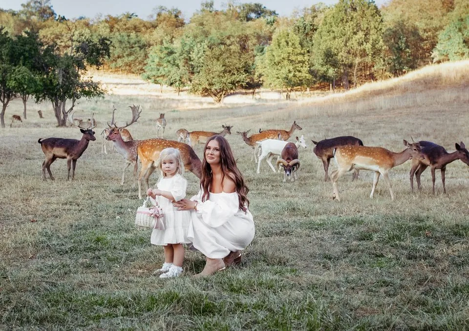 A magical scene with white-dressed figures surrounded by grazing deer in a meadow.