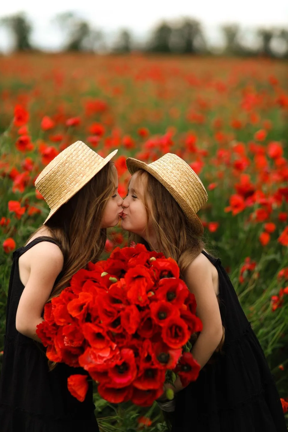 Two people in black dresses and straw hats sharing moment among red poppies.