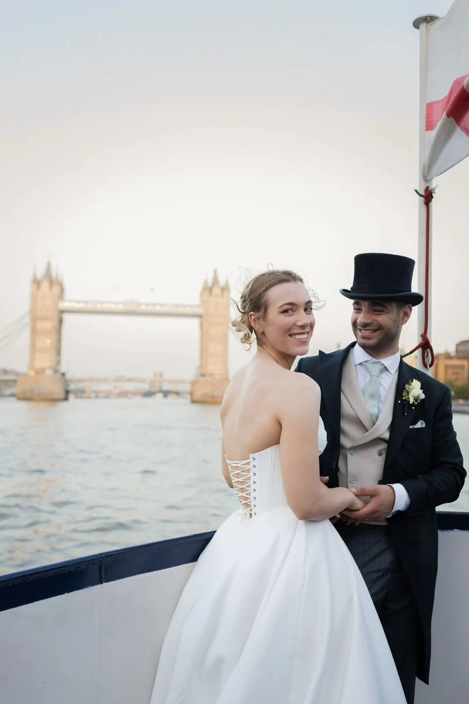 Bride and groom posing on a boat with Tower Bridge London in the background at sunset.