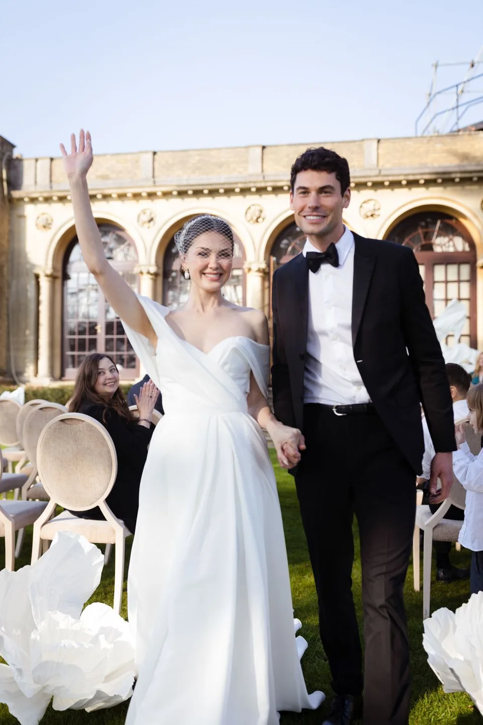 A newlywed couple celebrates during an outdoor wedding ceremony with white garden chairs and floral decorations.