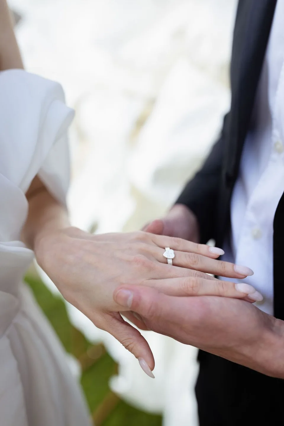 Close-up of hands exchanging wedding rings during a ceremony with elegant white dress and black suit visible.