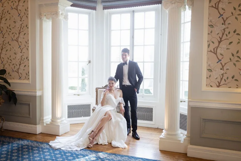 Elegant wedding scene in bright bay window room with ornate wallpaper and classic decor.