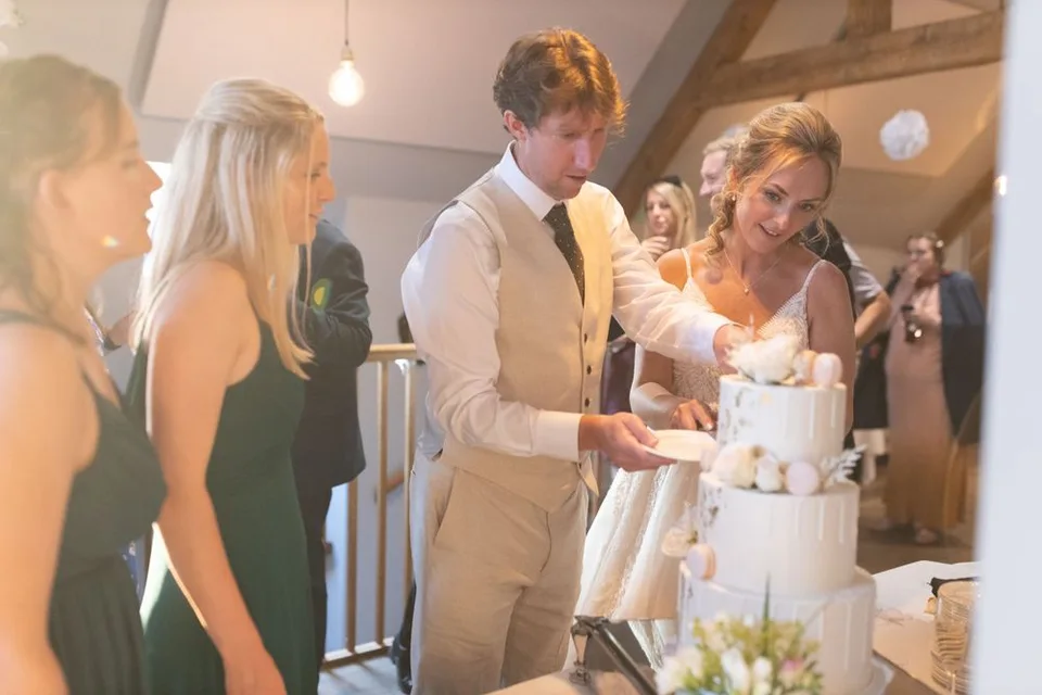 Wedding cake cutting ceremony in a rustic venue with exposed wooden beams.
