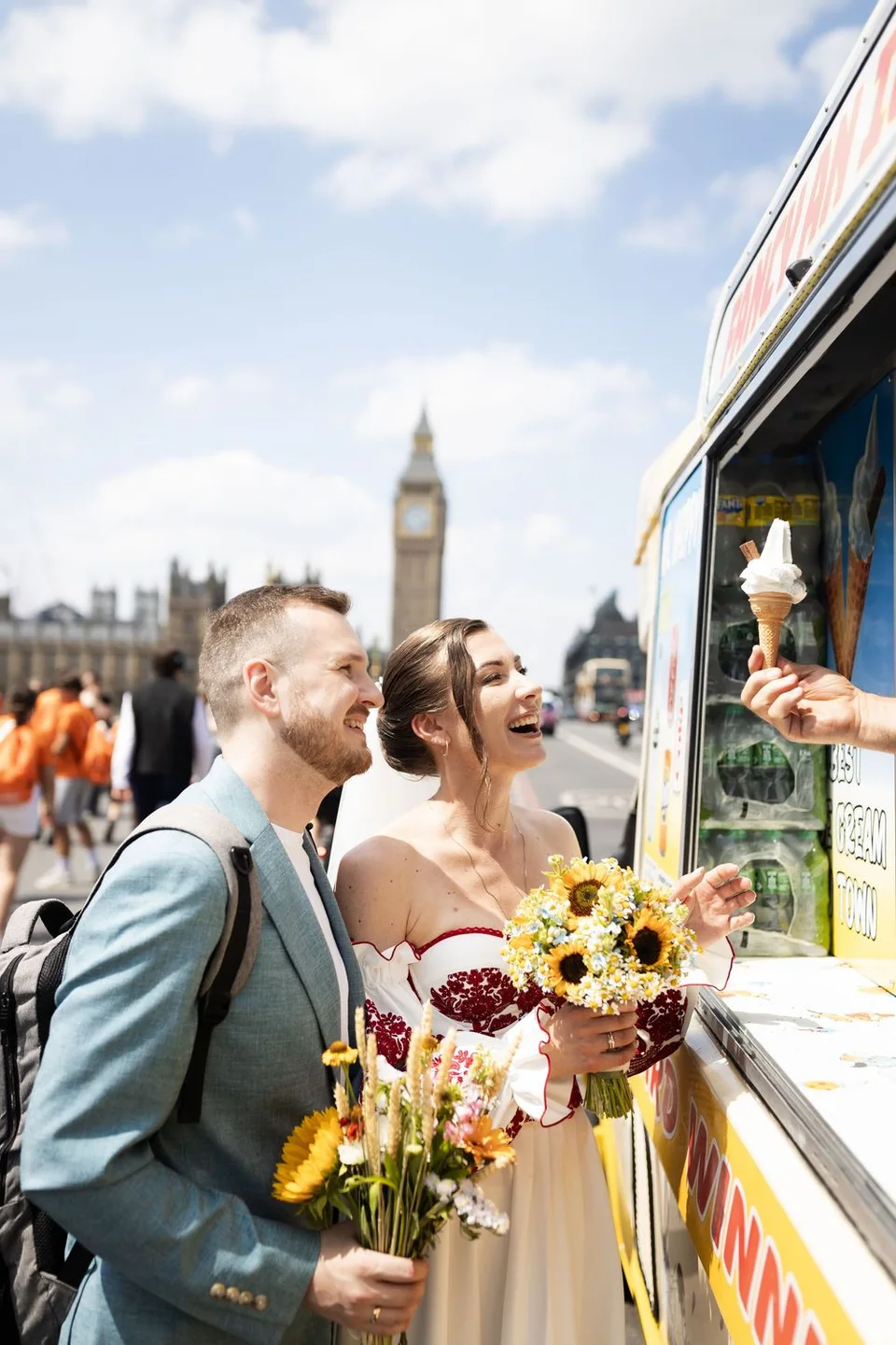 Newlyweds buying ice cream from a street vendor near Big Ben in London, bride holding sunflower bouquet.