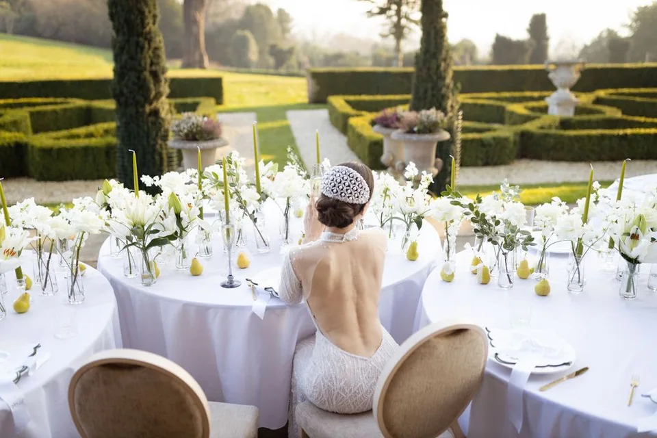 Outdoor wedding table setting with white flowers and elegant place settings overlooking manicured gardens.