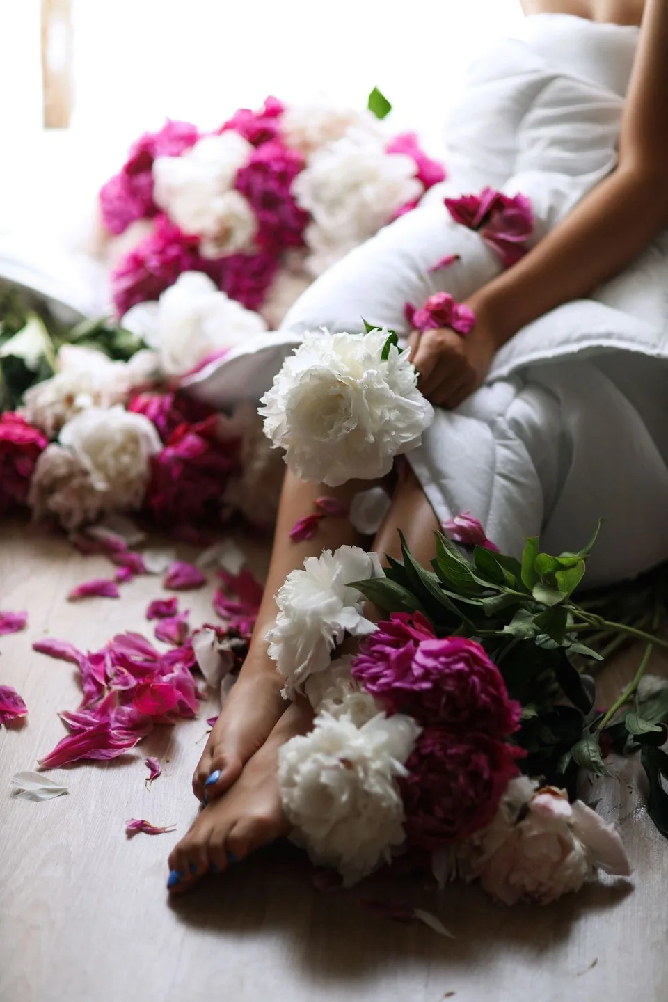 Artistic still life with scattered pink and white peonies around white fabric.