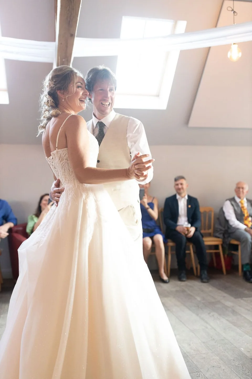 Joyful dance moment at indoor wedding reception with guests looking on.