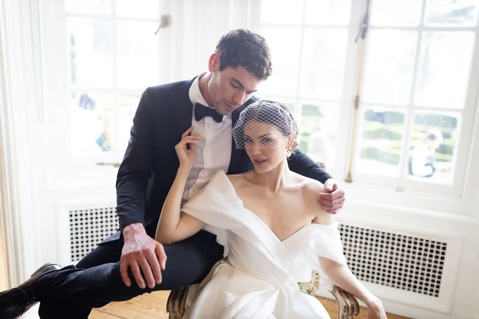 Tender wedding moment captured in sunlit room with classic decor.