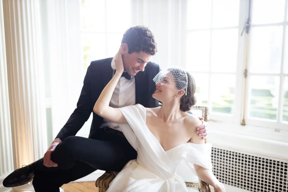Intimate wedding portrait by sunlit window showing playful dance-like pose.