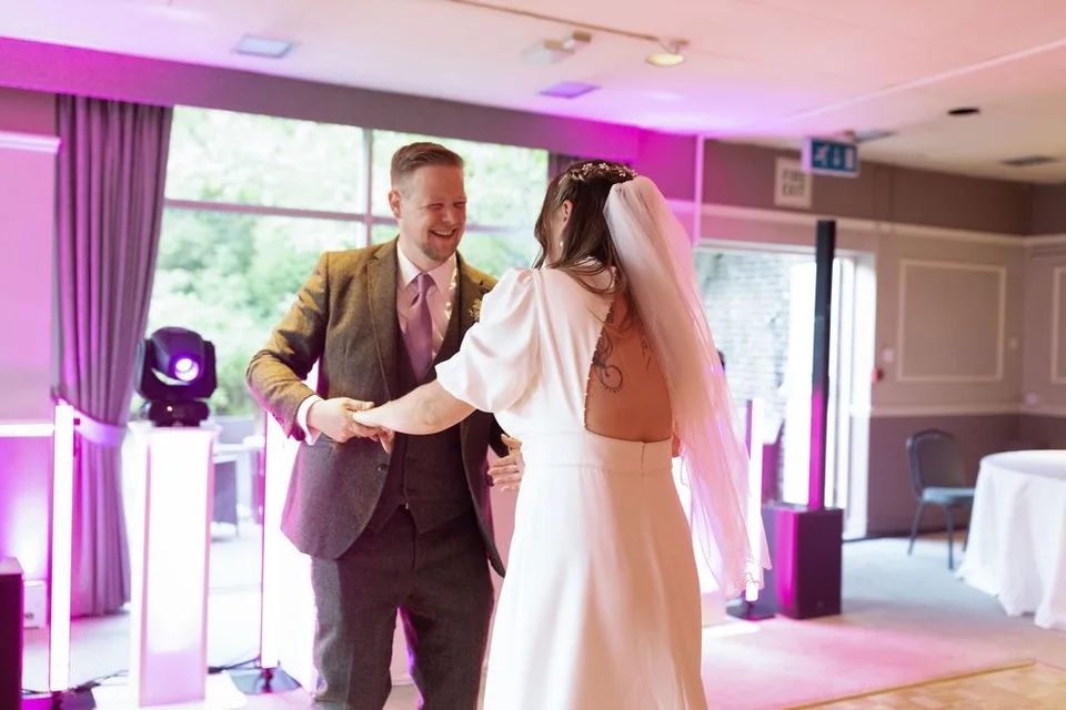A newlywed couple shares a tender moment during their first dance at their wedding reception with pink lighting.