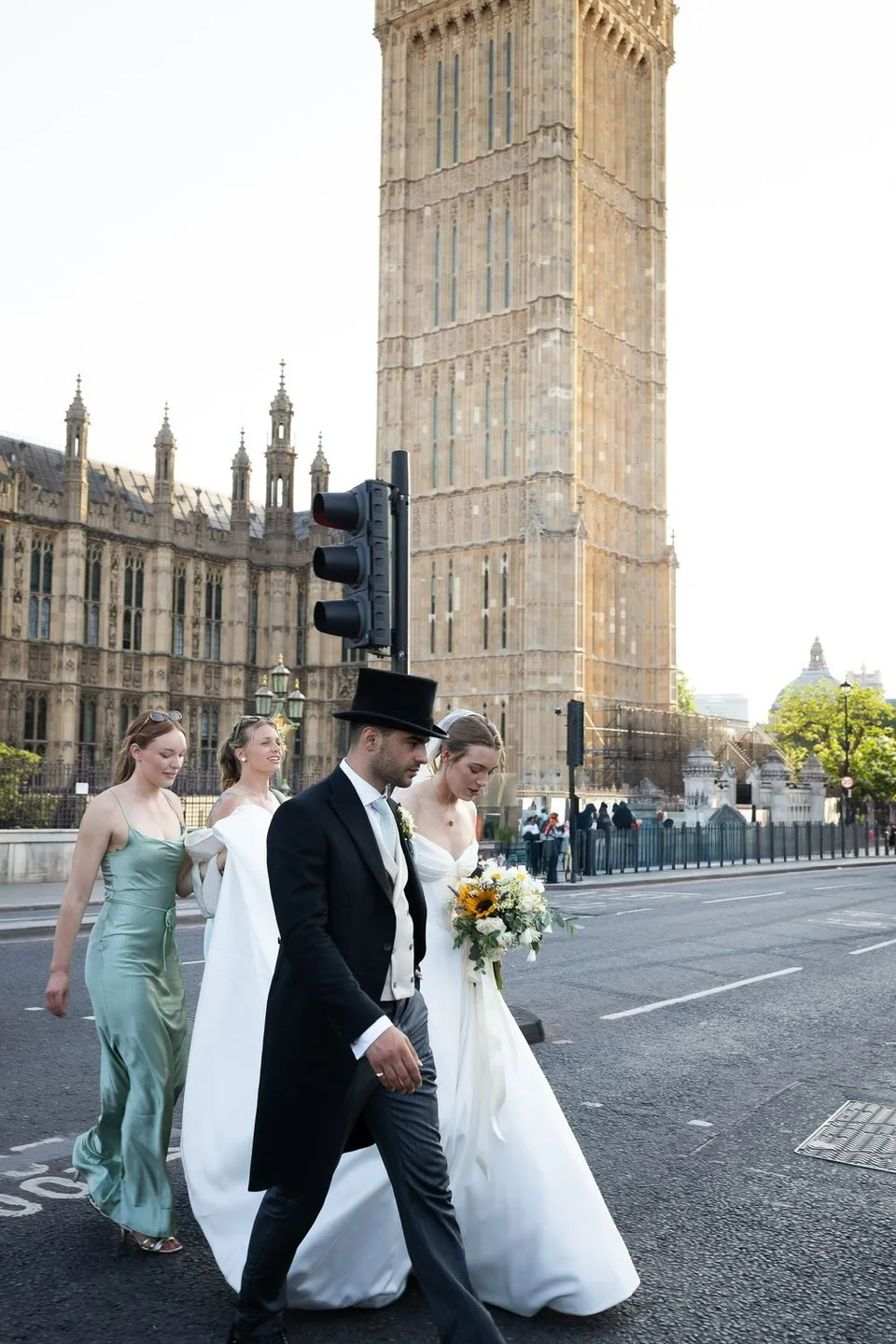 Wedding couple walks past Big Ben in London, bride in white gown with bouquet, groom in top hat and tails.