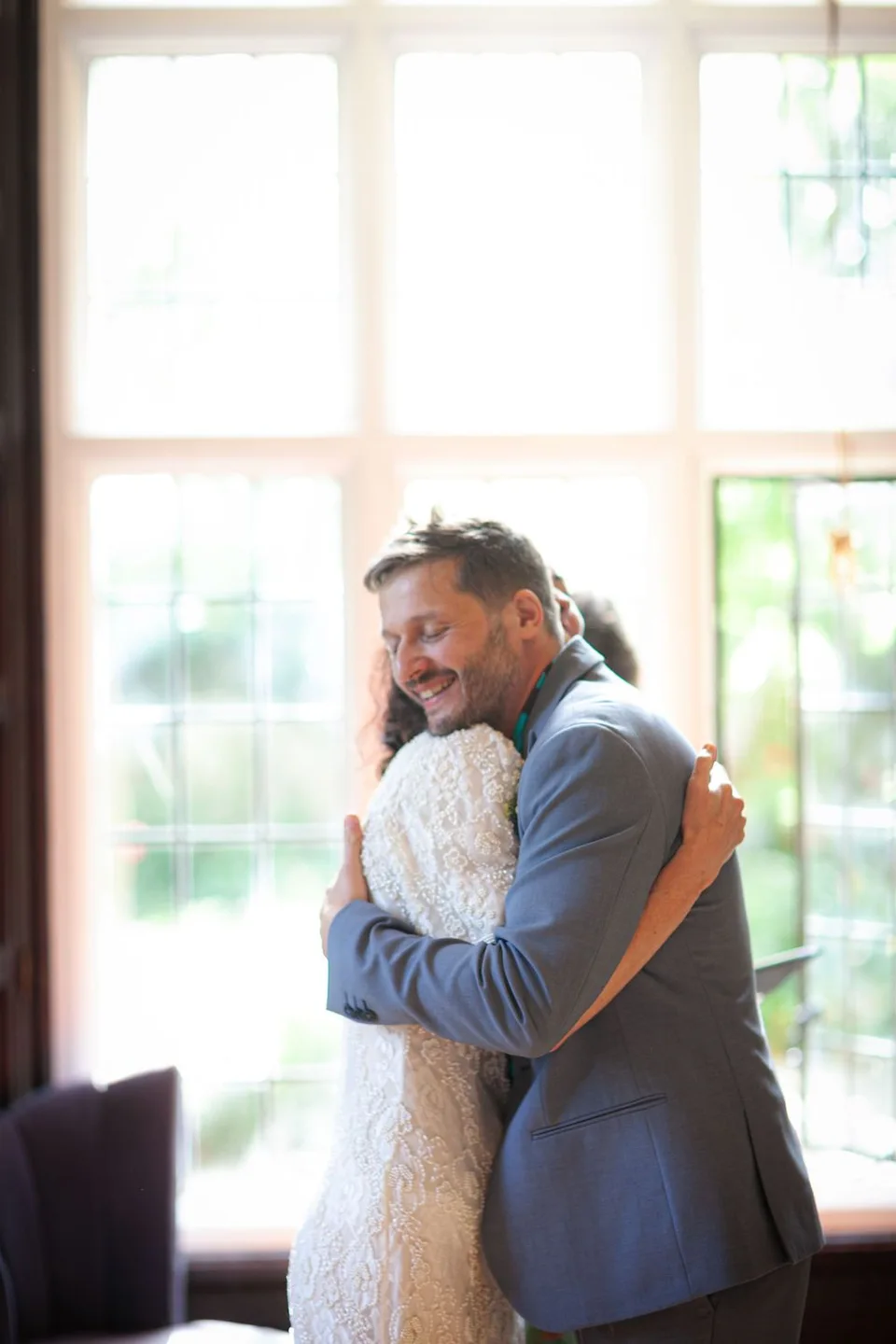 Tender embrace between wedding couple in sunlit indoor setting.