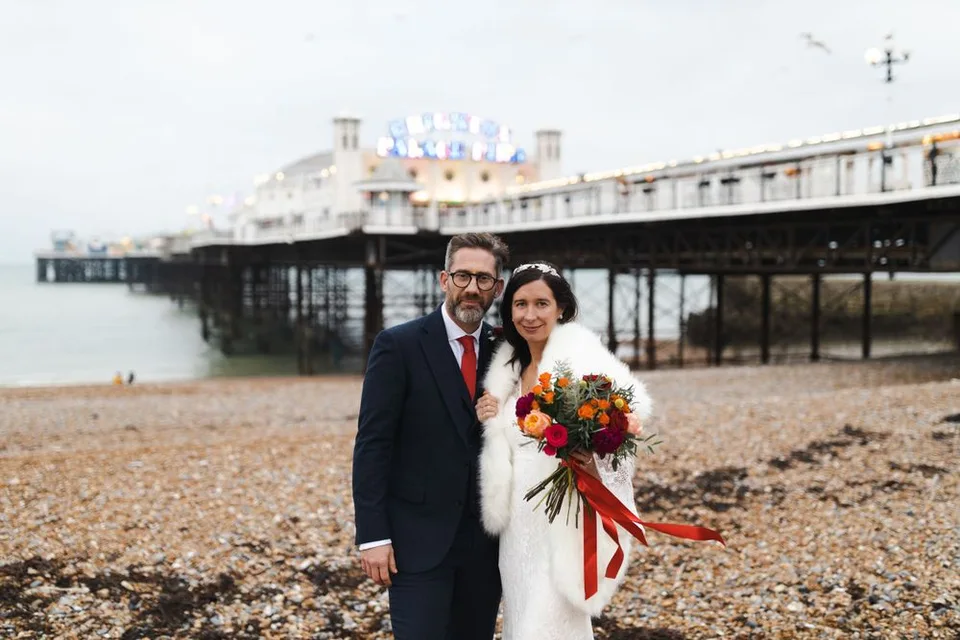 Wedding couple poses on Brighton beach with the famous pier in the background.