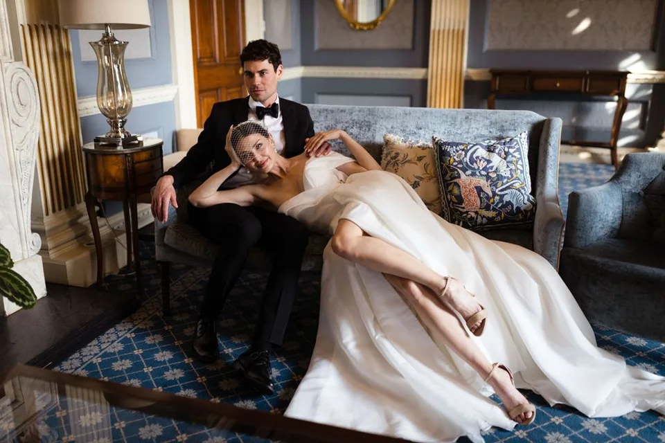 Romantic wedding couple lounges on vintage blue sofa in elegant interior setting.