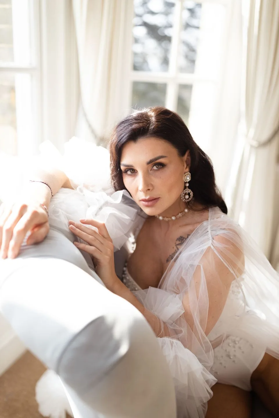 Romantic boudoir photography setup in a bright sunlit room with flowing white curtains and elegant decor.