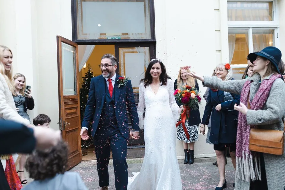 Wedding guests shower the newlyweds with confetti outside a historic building.