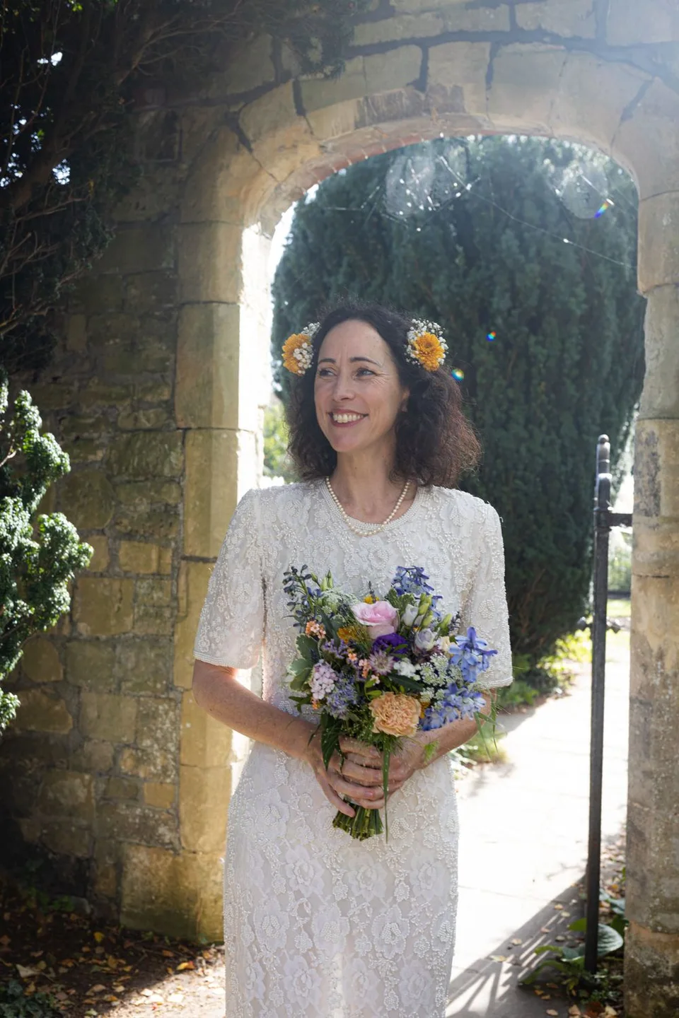 Beautiful bridal portrait under stone archway with wildflower bouquet.