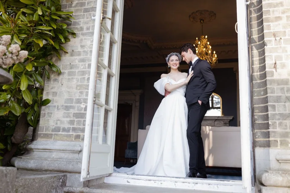 Romantic wedding couple poses in doorway of historic brick building with luxury interior.