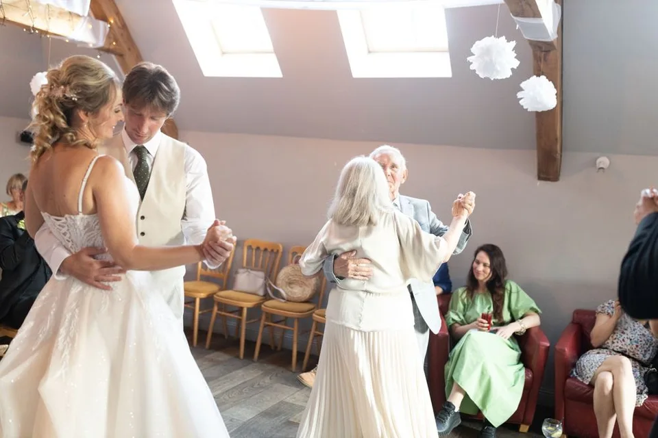 Wedding guests dance together during a joyful reception celebration in a sunlit venue.