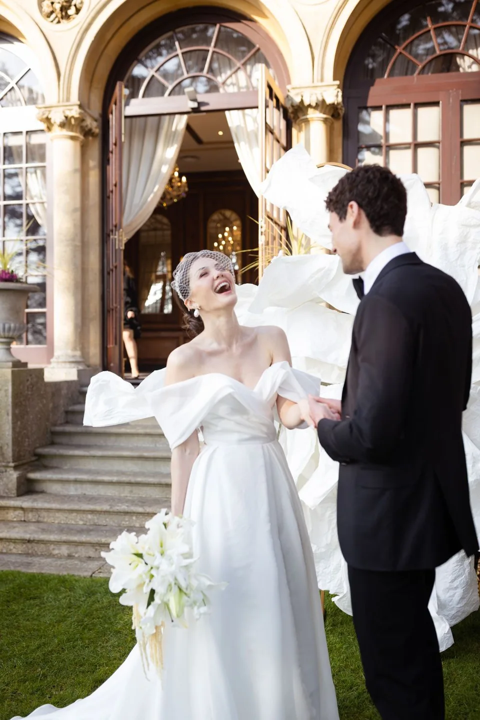 Joyful wedding moment captured under ornate arched entrance with white flowers.