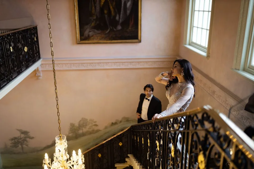 Romantic wedding photo of a couple descending an ornate staircase with chandelier and painted walls.