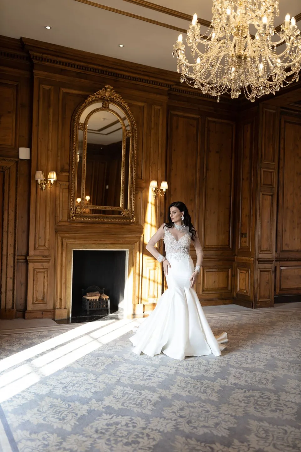 Elegant bridal portrait in ornate wood-paneled room with crystal chandelier and gilded mirror.
