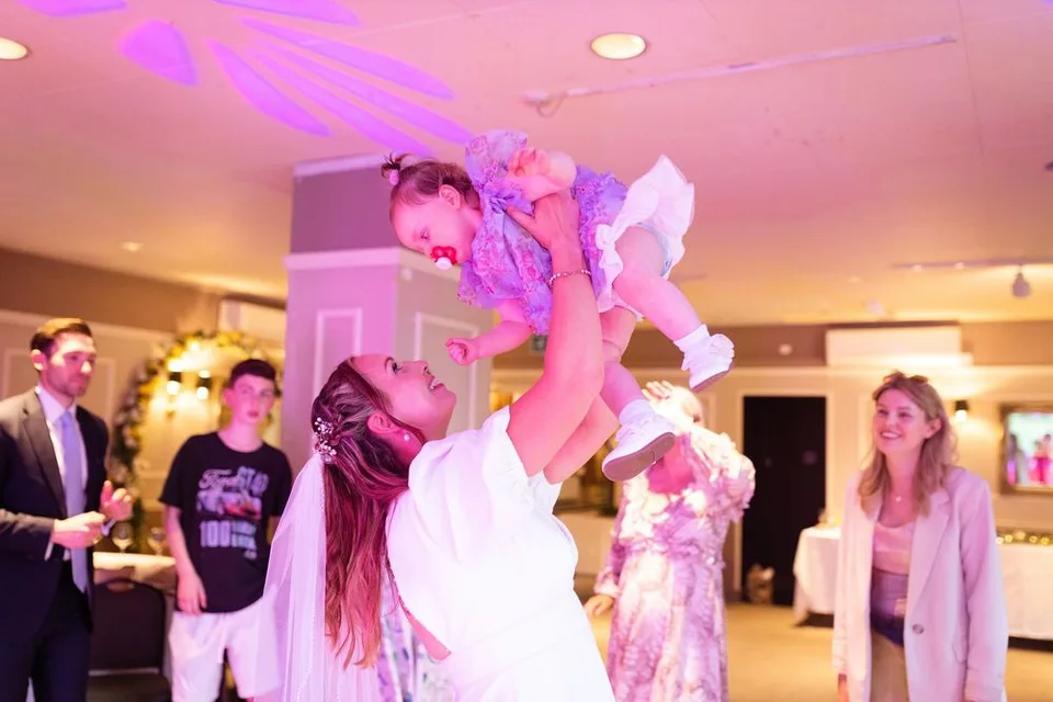 A person in purple dance attire is lifted up at an indoor dance celebration under pink and purple lighting.