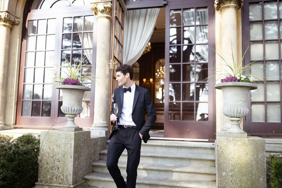 Formal attire against classic architectural backdrop with stone columns and potted plants.