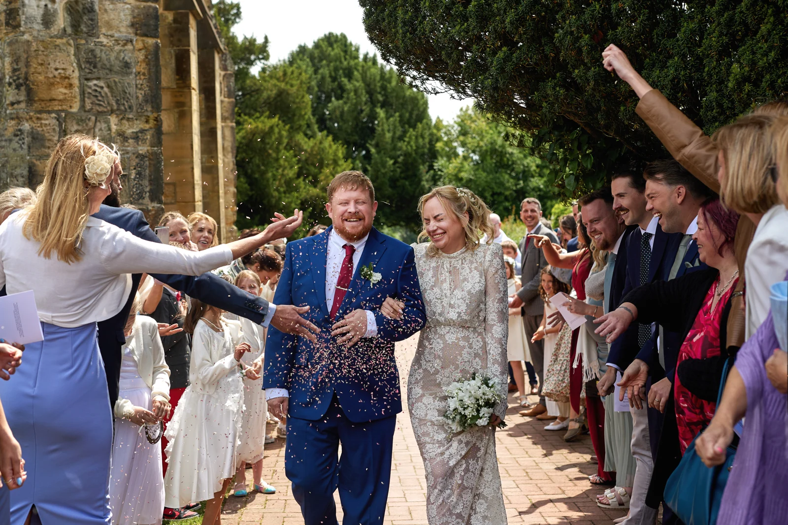 Kate and Rob walking through confetti outside Holy Trinity Church in Cuckfield.