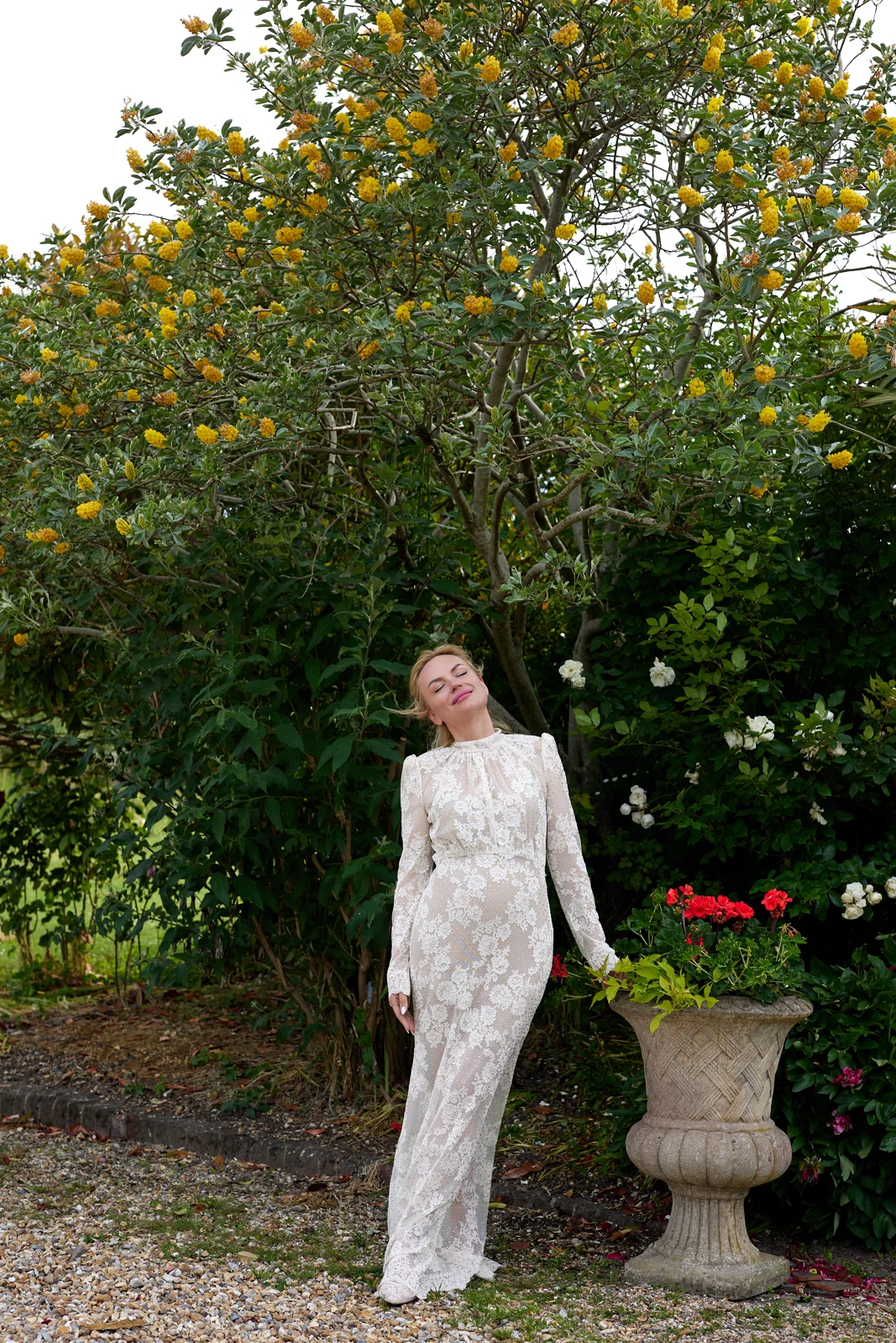 Kate in her wedding dress beneath flowering trees in a garden.
