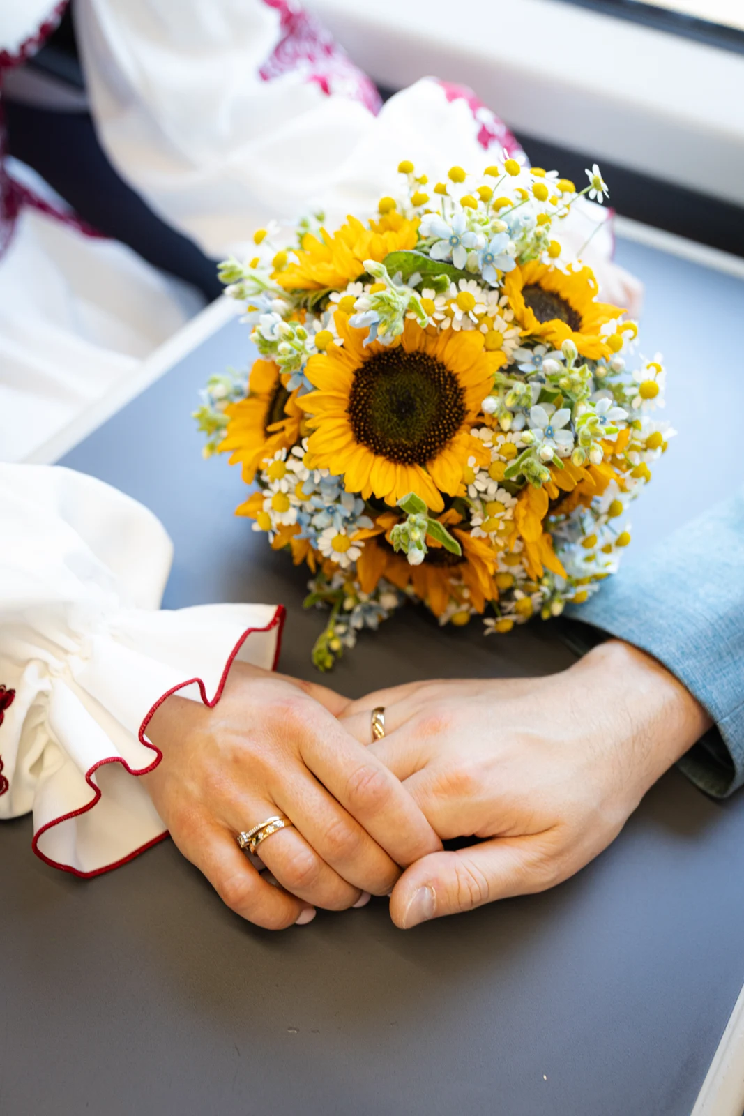Lena and Arturs holding hands beside their sunflower bouquet on the train.