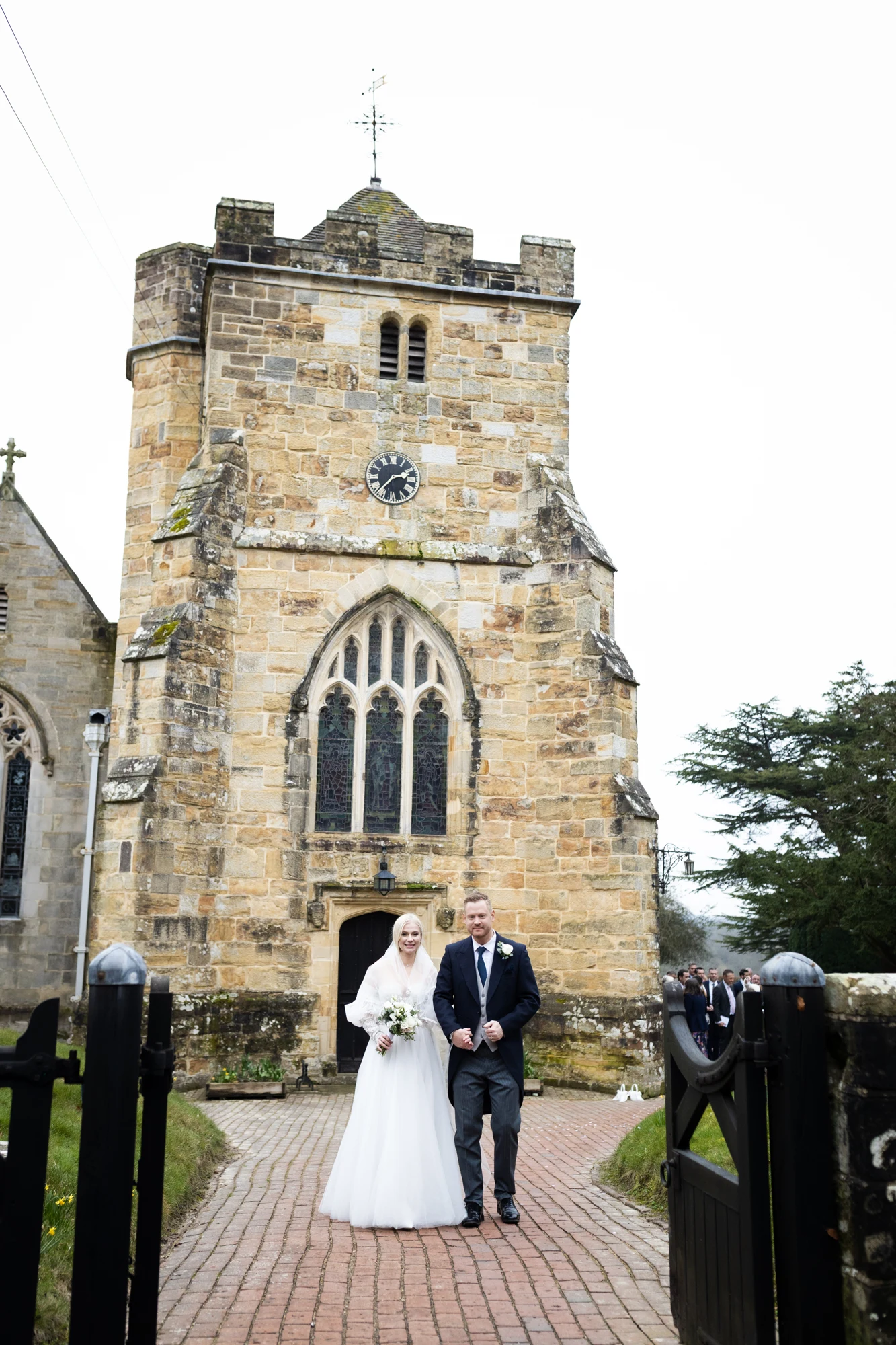 A newly married couple walking through the gates outside a stone church.