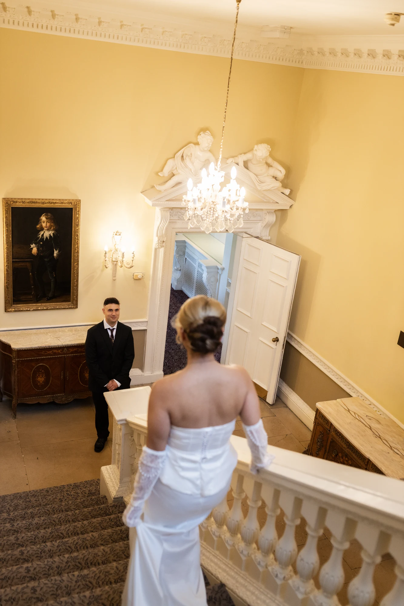A bride descending a grand staircase towards the groom waiting below.